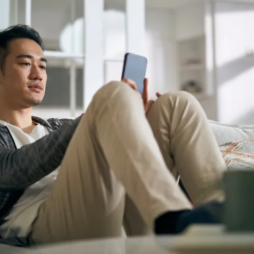 Man sits on the couch with a concerned look on his face while looking at a smartphone
